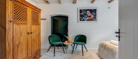 Une pièce comprenant une armoire en bois, deux chaises vertes, une petite table, un tableau et un lit.
