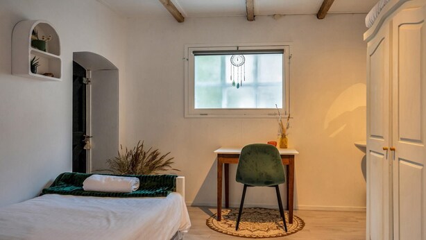 A bedroom with a bed, a desk, a chair, a window, and a wardrobe.