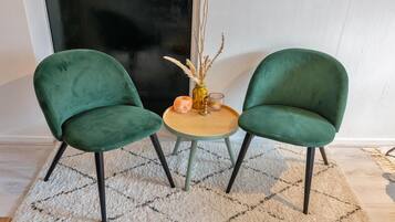 Deux fauteuils verts à revêtement en tissu, avec des pieds noirs, une petite table ronde en bois et un vase contenant des plantes séchées.