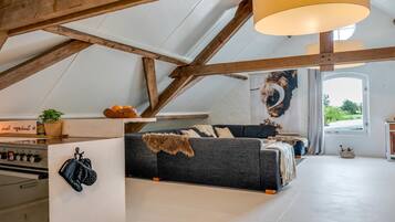 Un espace de vie de style loft avec des poutres apparentes, un canapé et une grande fenêtre.