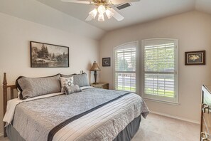 Un dormitorio con cama, ventilador de techo, ventana con persianas y un cuadro en la pared.