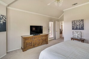Ein Schlafzimmer mit einem großen Bett, einem Fernseher auf einer Holzkommode, einer Tür zu einem anderen Raum und einem Deckenventilator.