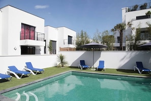 A modern outdoor pool area with blue lounge chairs and a clear blue pool.