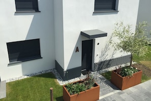 A modern building with a flat facade, a small entrance, and two rectangular planters with plants.