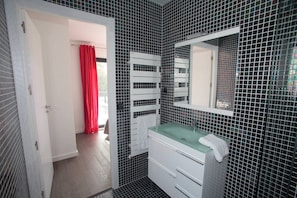 A bathroom with a glass sink, white cabinets, and a tiled wall.