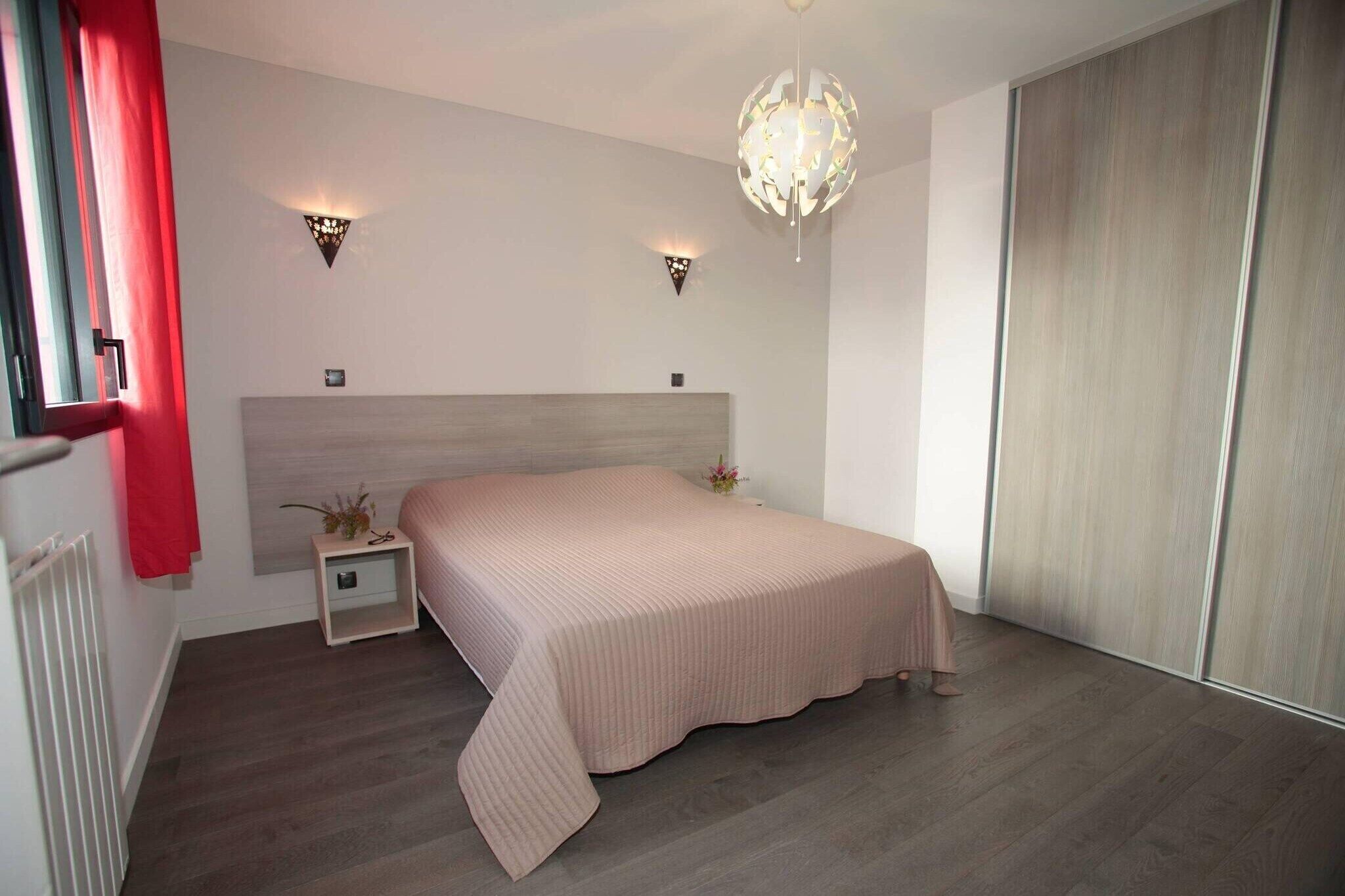 Une chambre à coucher avec un lit, des tables de chevet, une commode, un rideau rouge, un lustre et une porte coulissante.