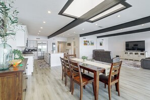 A modern kitchen with white cabinets, a dining area with a wooden table and chairs, and a living room with a sofa and a TV. - Colorado River Family Escape in Bullhead City (Bullhead City)