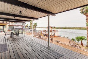 Eine Holzterrasse mit Gartenmöbeln, die auf ein Gewässer und eine entfernte Landschaft blickt.