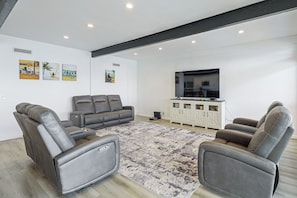 Un salon moderne avec un canapé gris, un téléviseur à écran plat et des œuvres d’art accrochées aux murs.