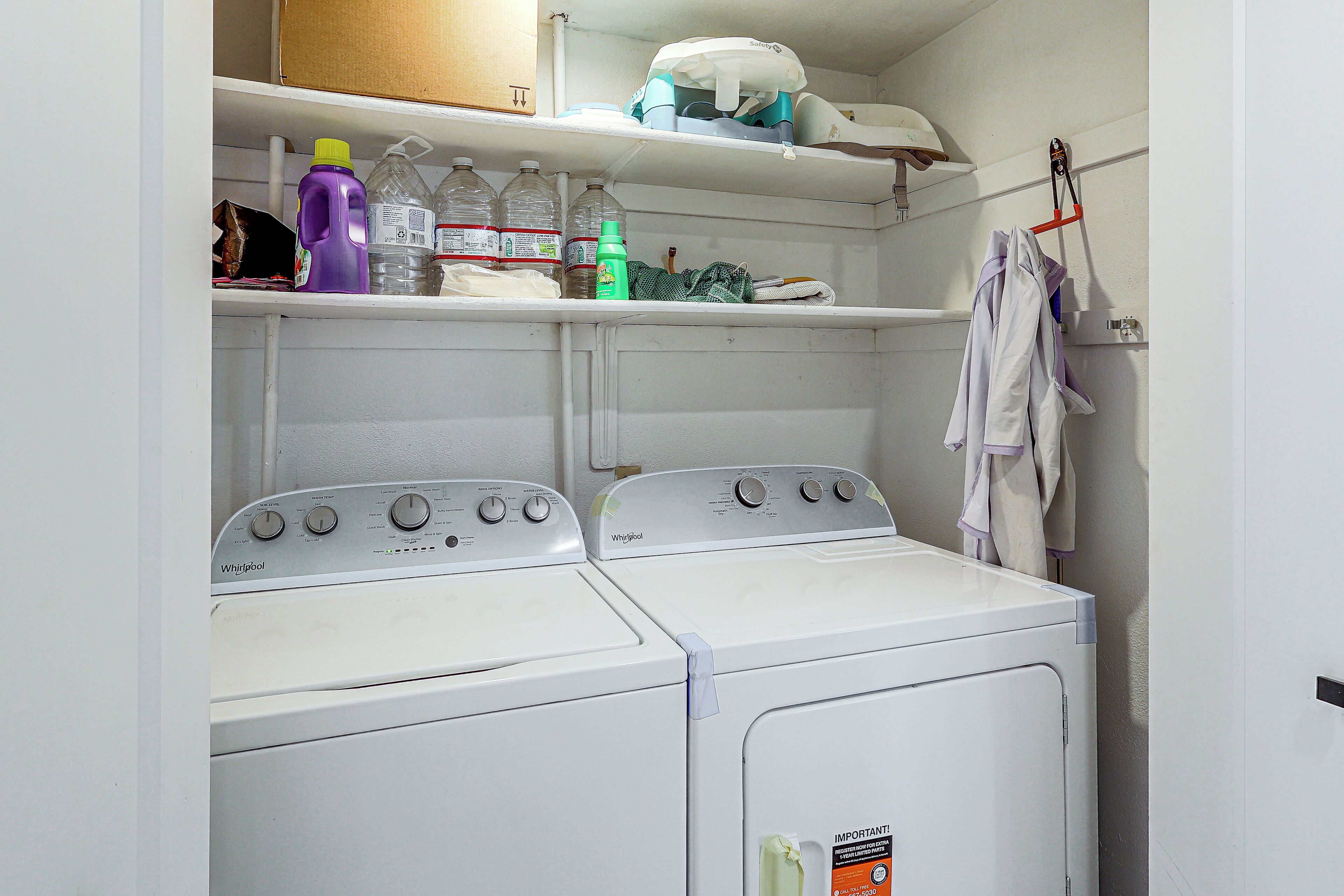 Ein Waschraum mit zwei Whirlpool-Waschmaschinen, Regalen darüber mit Reinigungsmitteln und einem Wäscheständer mit Handtüchern.