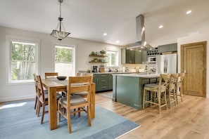 A modern kitchen with a central island, wooden dining table with chairs, and large windows allowing natural light. - Newly Built Wooded Getaway in Grand Junction (Grand Junction)