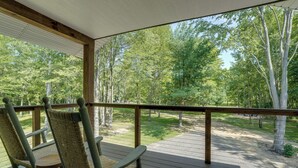 A covered outdoor area with two wicker chairs and a wooden table, overlooking a wooded area. - Newly Built Wooded Getaway in Grand Junction (Grand Junction)