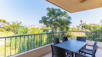 Ein Balkon mit Tisch und Stühlen, der auf eine grüne Landschaft mit Bäumen und Gebäuden blickt.