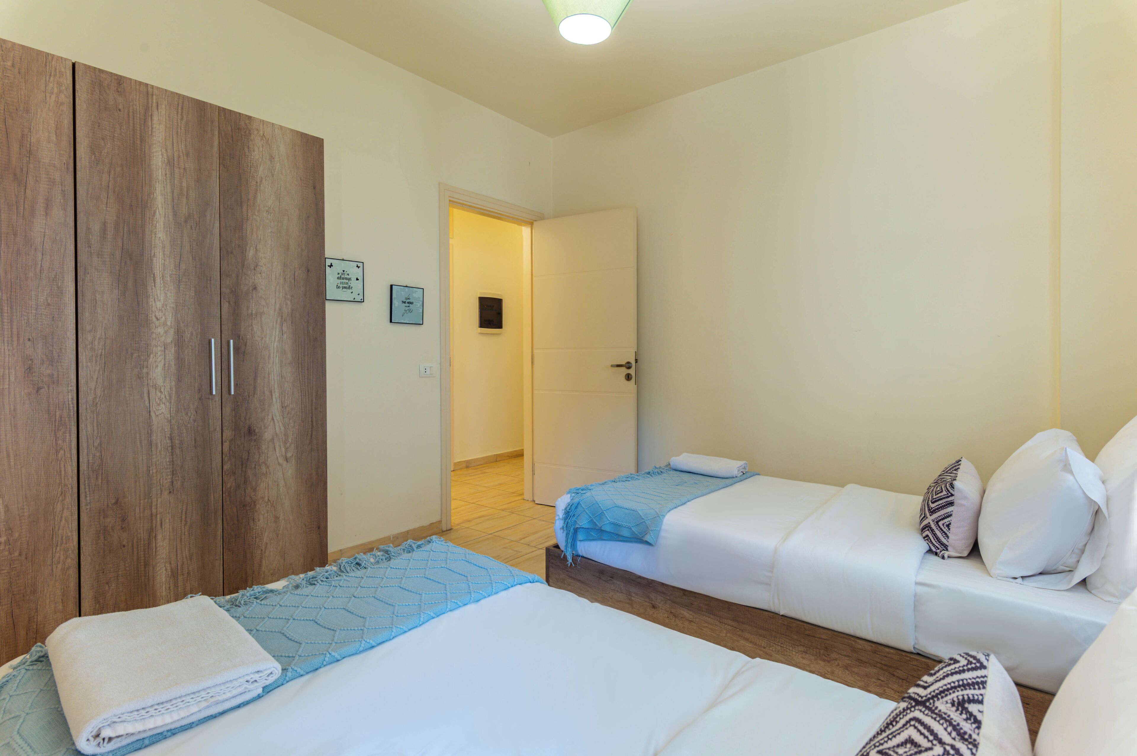 A hotel room with two beds, a wardrobe, and a door leading to another room.