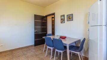 Un pequeño comedor con una mesa, cuatro sillas, un refrigerador y dos platos decorativos en la pared.