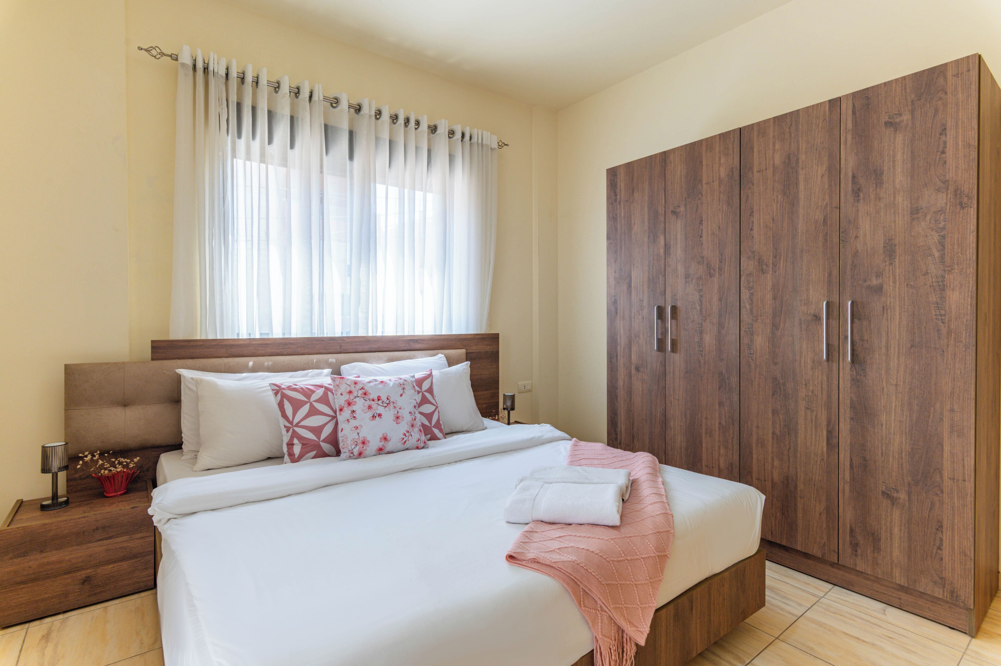 Un dormitorio con cama, mesitas de noche, armario y ventana con cortinas.