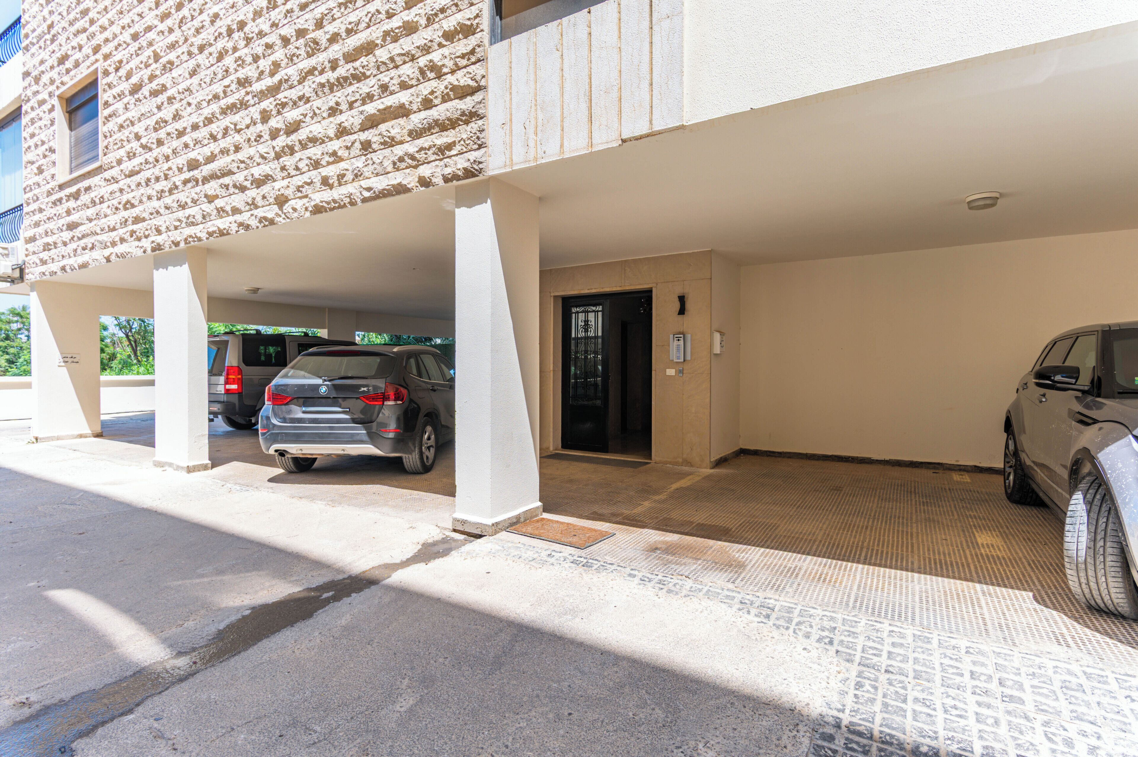 A parking area with a covered entrance, a car parked inside, and a building facade with a textured wall.