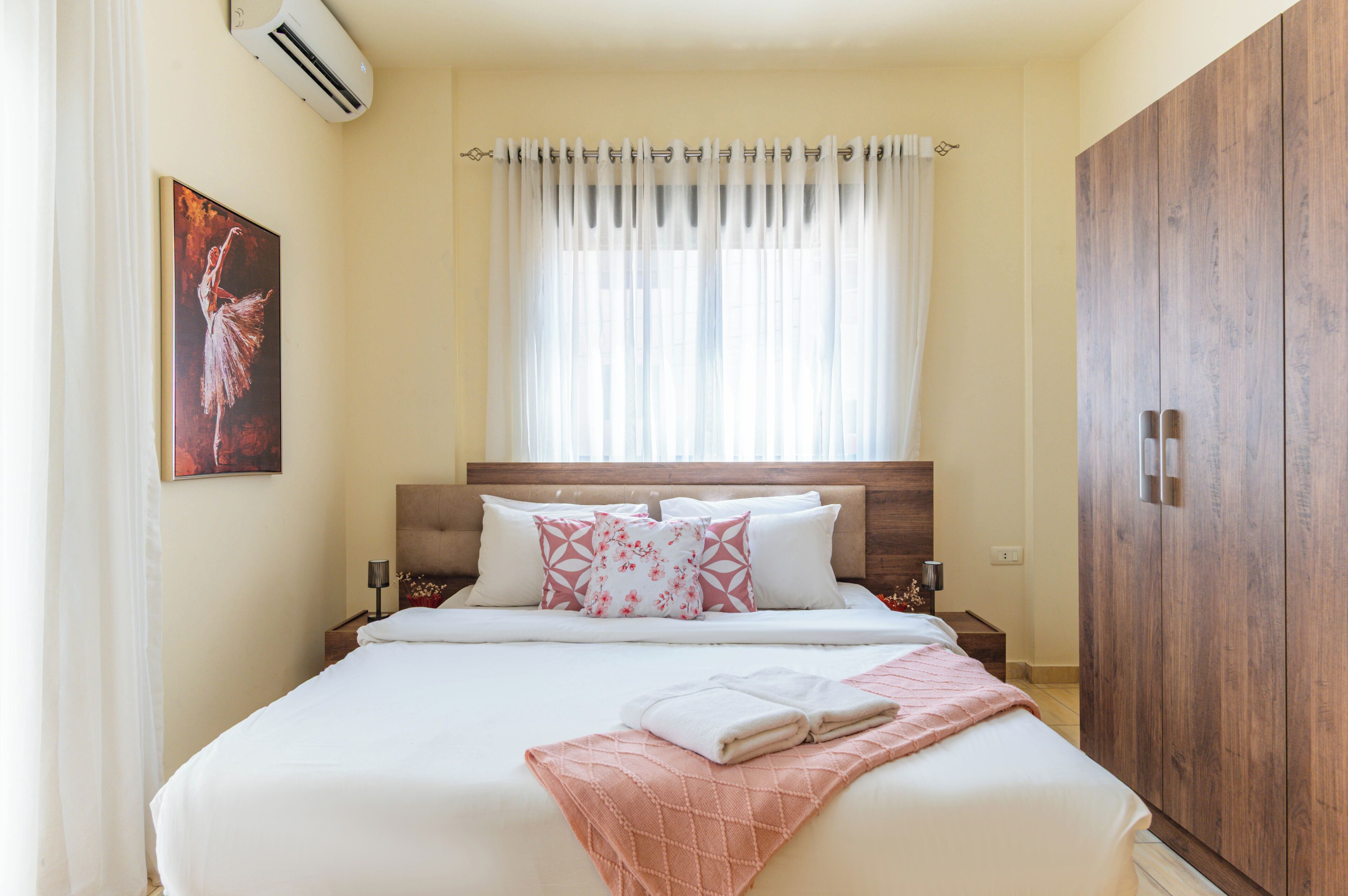 Una habitación de hotel con cama, cabecera, ventana con cortinas, armario y aire acondicionado de pared.