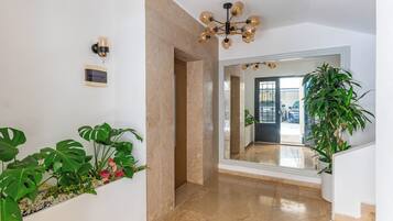 Un pasillo con piso de mármol, una lámpara en el techo y un espejo grande que refleja una puerta y un vehículo en el exterior.
