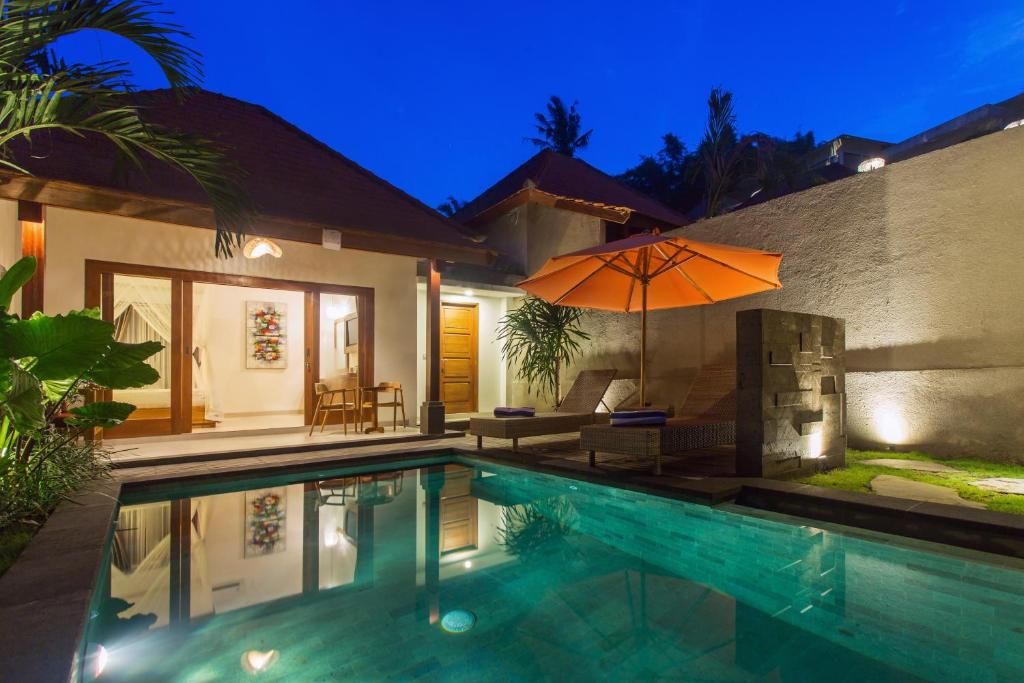 A swimming pool with a lounge area, a covered seating area, and a building with a door and windows.