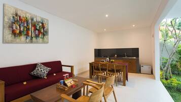 Ein moderner Wohnbereich mit einem roten Sofa, einem Holzesstisch und Stühlen. Eine Küchenzeile mit schwarzer Arbeitsplatte und Kühlschrank ist sichtbar.
