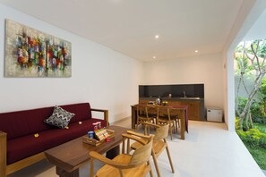 Un espacio habitable moderno con un sofá rojo, una mesa de comedor de madera y sillas. Se ve un área de cocina con una encimera negra y un refrigerador.