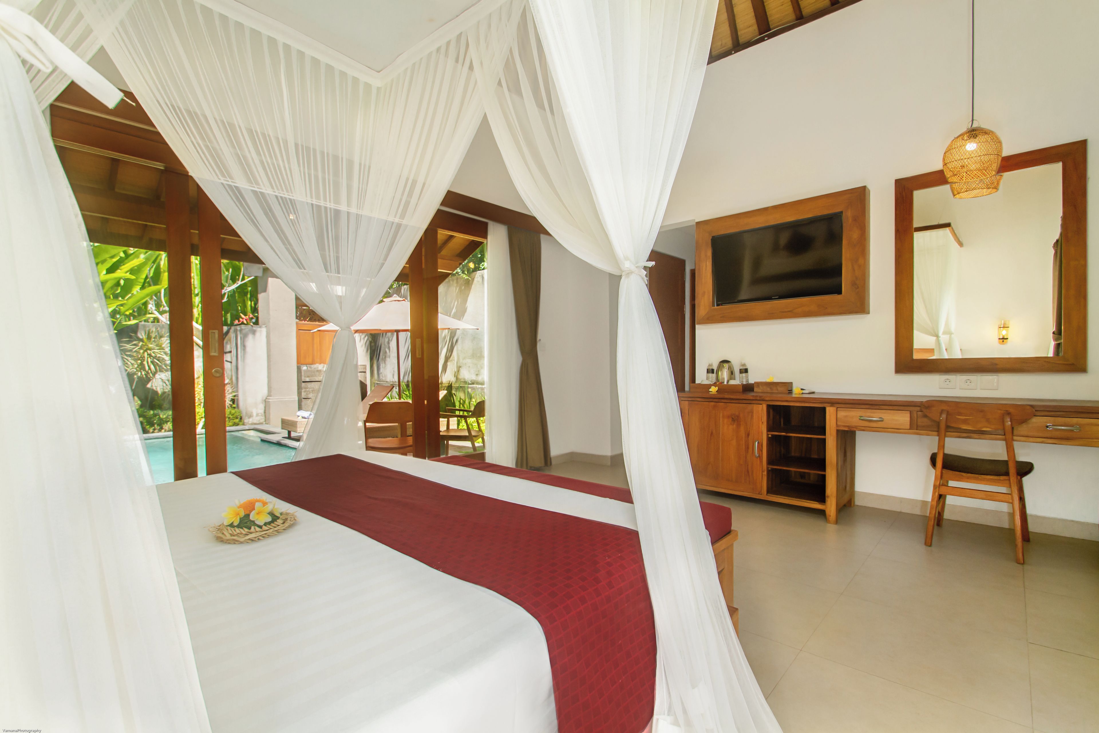 A bedroom with a bed, a desk, a mirror, and a view of an outdoor swimming pool.