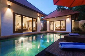 Un área junto a la piscina con una piscina cristalina, sillas de descanso y un espacio de estar techado.