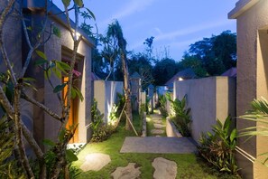 Uma trilha leva a um edifício de design moderno, cercado por vegetação exuberante e palmeiras.