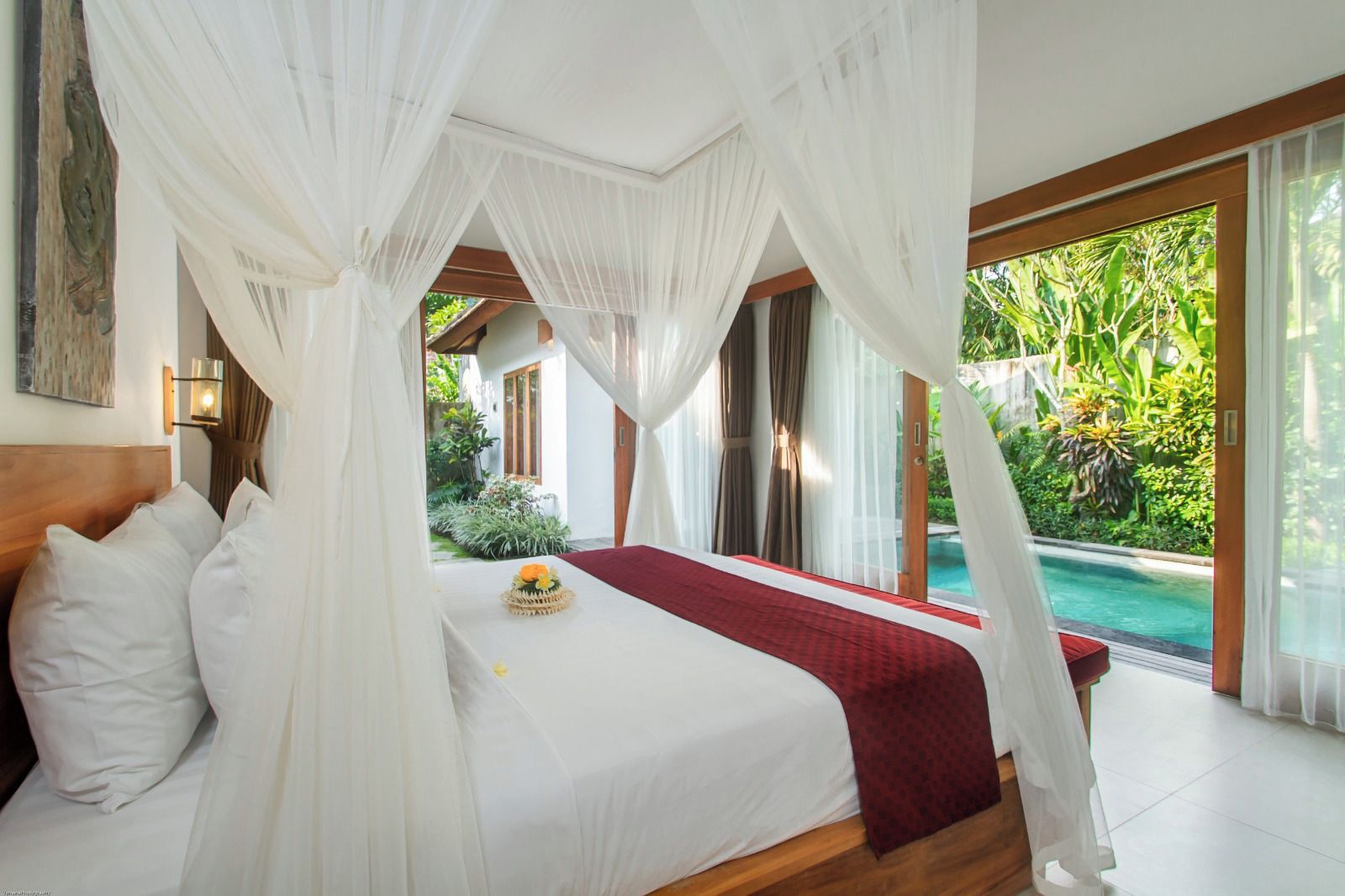A bedroom with a canopy bed, a view of a swimming pool, and a tropical garden.