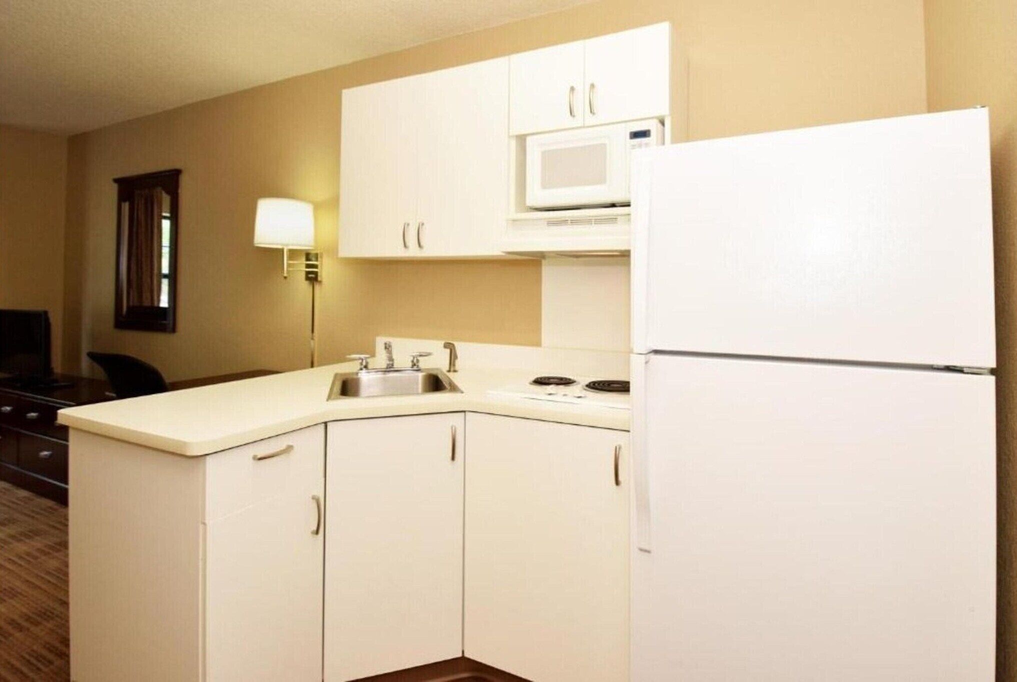 A compact kitchen with white cabinets, a microwave, a sink, and a refrigerator.