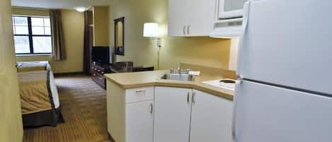 A compact hotel room with a kitchenette, a bed, a television, and a window with curtains.