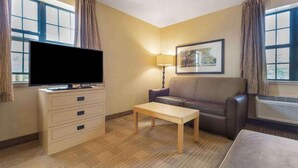 Habitación de hotel con televisor de pantalla plana, sofá, una mesita, lámpara y un cuadro en la pared.