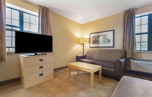Ein Hotelzimmer mit Flachbildfernseher, einer Sitzecke, einem kleinen Tisch, einer Lampe und einem gerahmten Bild an der Wand.