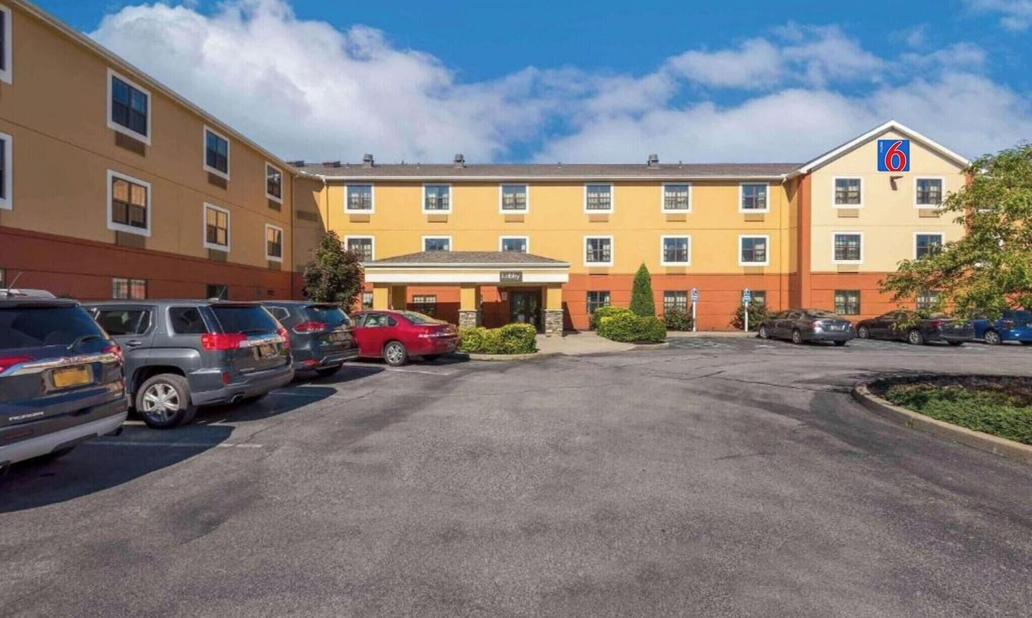 A hotel with a parking lot, multiple cars, and a clear sky.