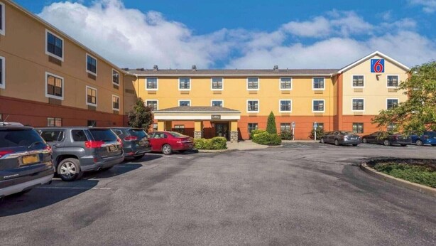 Un hotel con aparcamiento, varios coches y cielo despejado.