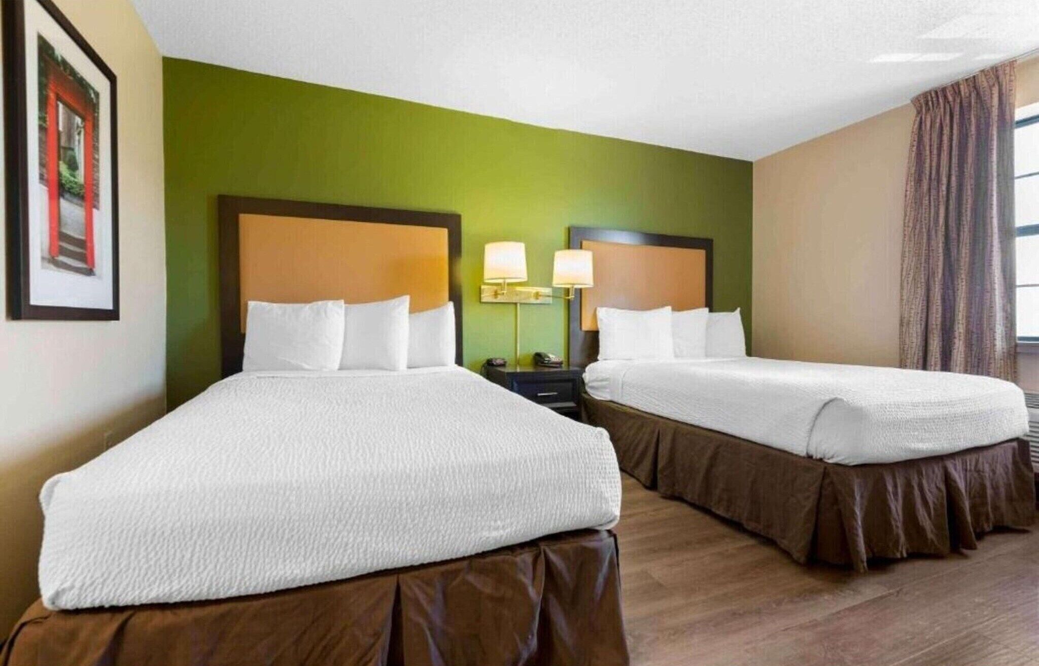 A hotel room with two beds, green walls, and a window with curtains.