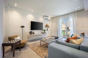 Ein modernes Wohnzimmer mit Flachbildfernseher, einer Couch, einem Couchtisch und einer Lampe.