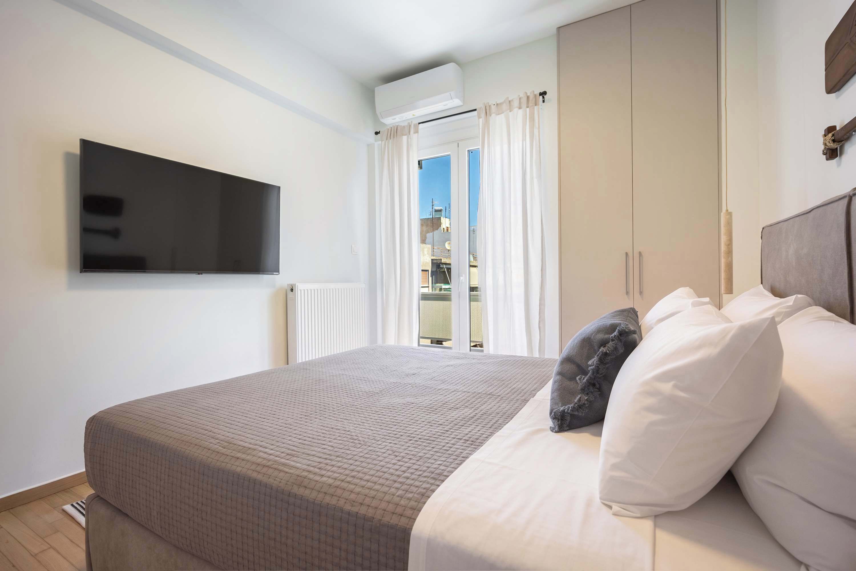 A bedroom with a bed, a television mounted on the wall, and a window with curtains.