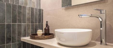 A modern bathroom with a large vessel sink, a mirror, a toilet, and a trash bin.