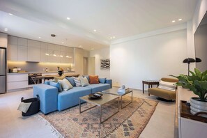 Un salon moderne avec un canapé bleu, une table basse et une cuisine en arrière-plan.