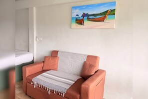 A room with a sofa, a painting of boats on a beach, and a bed. - Serene 1-bedroom apartment with AC in vibrant Rawai (Rawai)