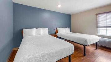 Une chambre avec deux lits simples, un plancher en bois, un mur d’accent bleu et une fenêtre avec des stores.