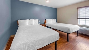 Dos camas individuales en una habitación con suelo de madera, una pared de acento azul y una ventana con persianas.