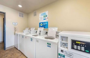 A laundry facility with five washers and dryers, a phone, and a poster advertising easier laundry. - 2 Full Beds | Smoking, Micfridge (Norman)
