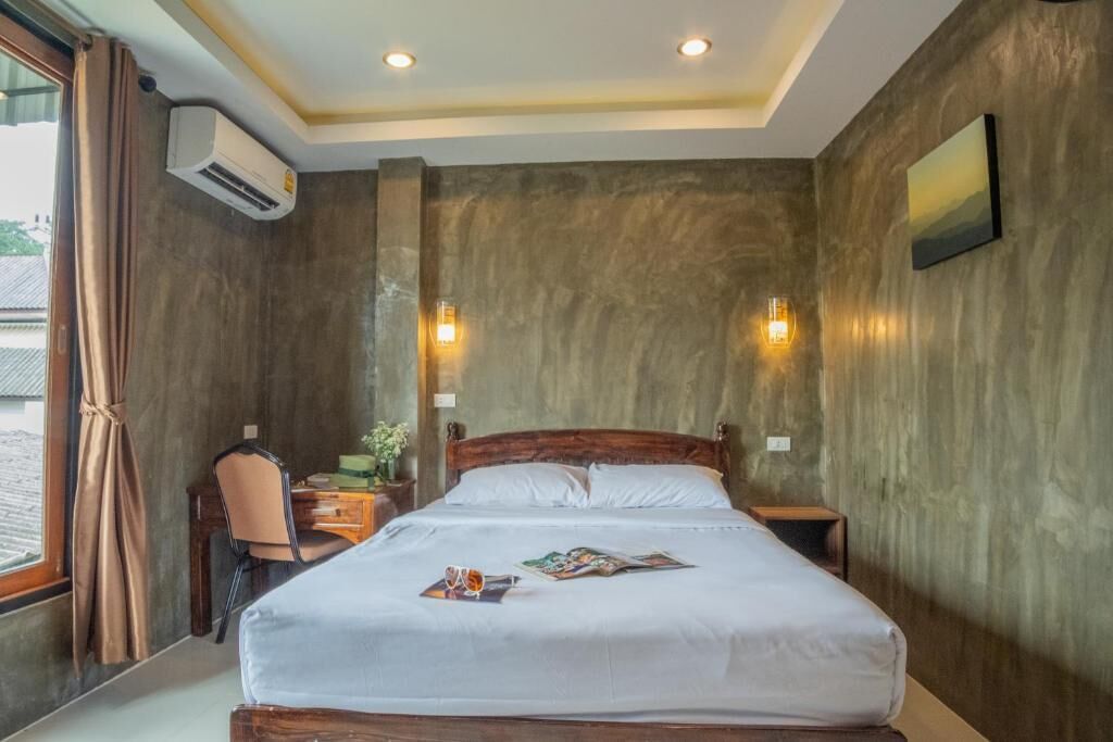 A hotel room with a large bed, a desk, and a chair. There is an air conditioning unit on the wall, and two wall-mounted lights.