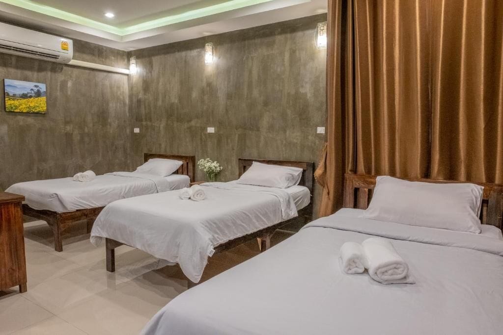 A hotel room with three beds, a wooden headboard, a small table, and an air conditioning unit.
