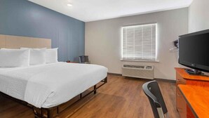 Ein Hotelzimmer mit Bett, Schreibtisch, Stuhl, Fernseher und einem Fenster mit Jalousien.
