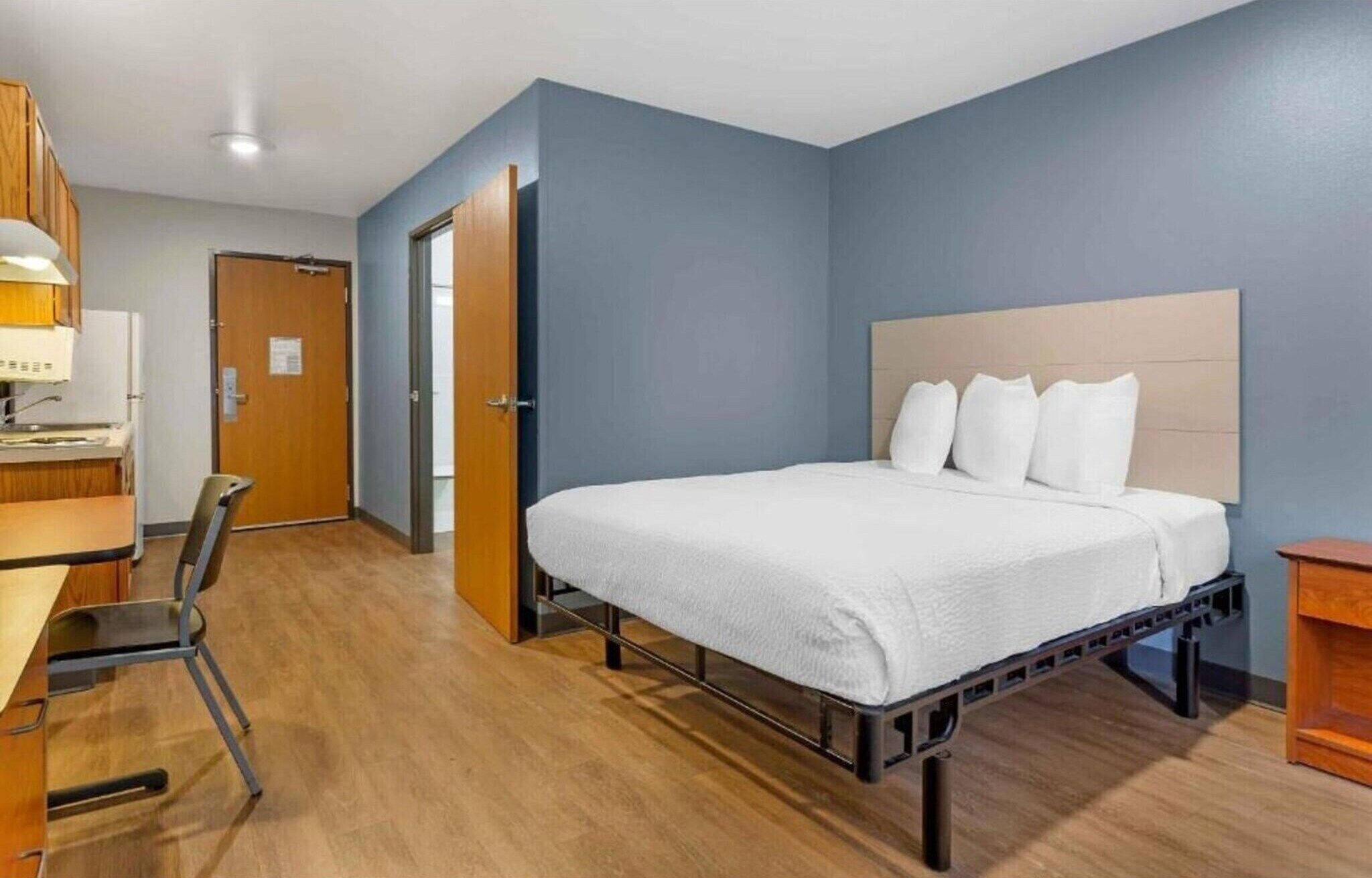 Una habitación de hotel con cama, escritorio, silla y una puerta que da a otra habitación.