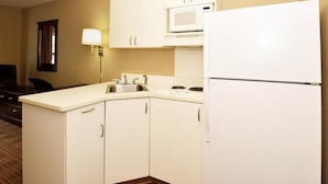 Una cocina compacta con armarios blancos, un microondas, un lavamanos y un refrigerador.